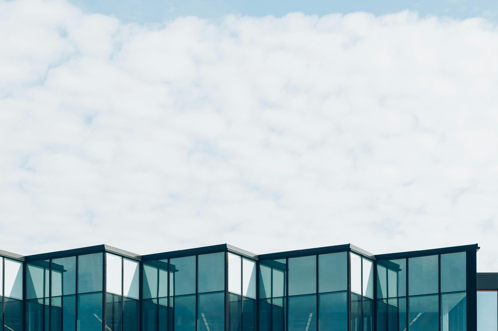 Low angle view of a modern glass building with a cloudy sky background, showcasing contemporary architecture.