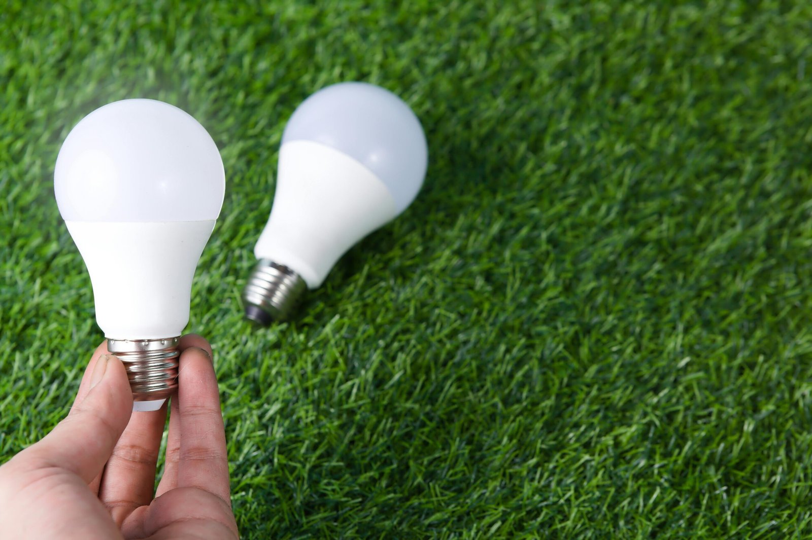 Hand holding LED light bulb on a grass surface, representing energy efficiency.